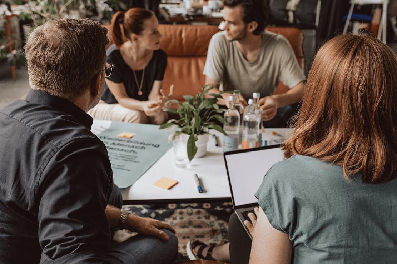Ein Mitarbeiter macht Notizen zu einem Gespräch unter vier Personen in einer gemütlichen Sofa-Umgebung